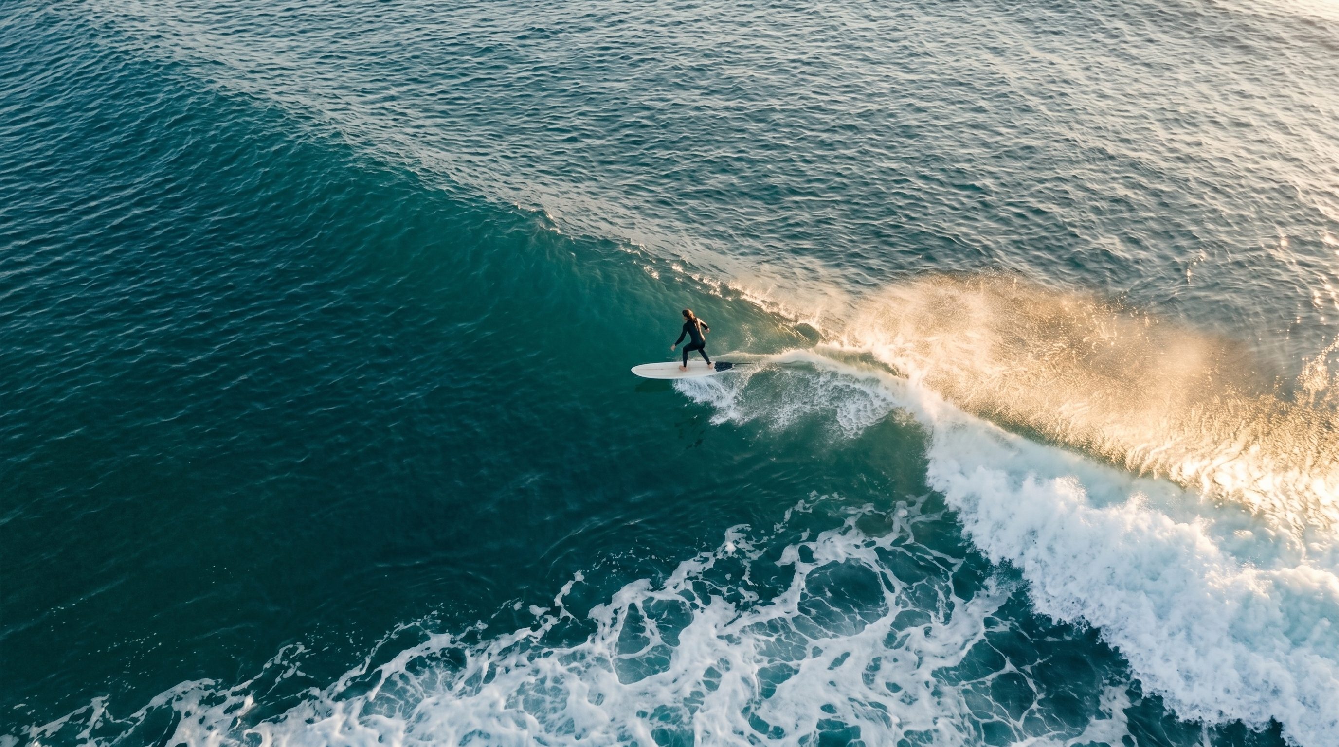 Vue aérienne d'un surfeur prenant une vague, écume blanche en diagonale, mer turquoise