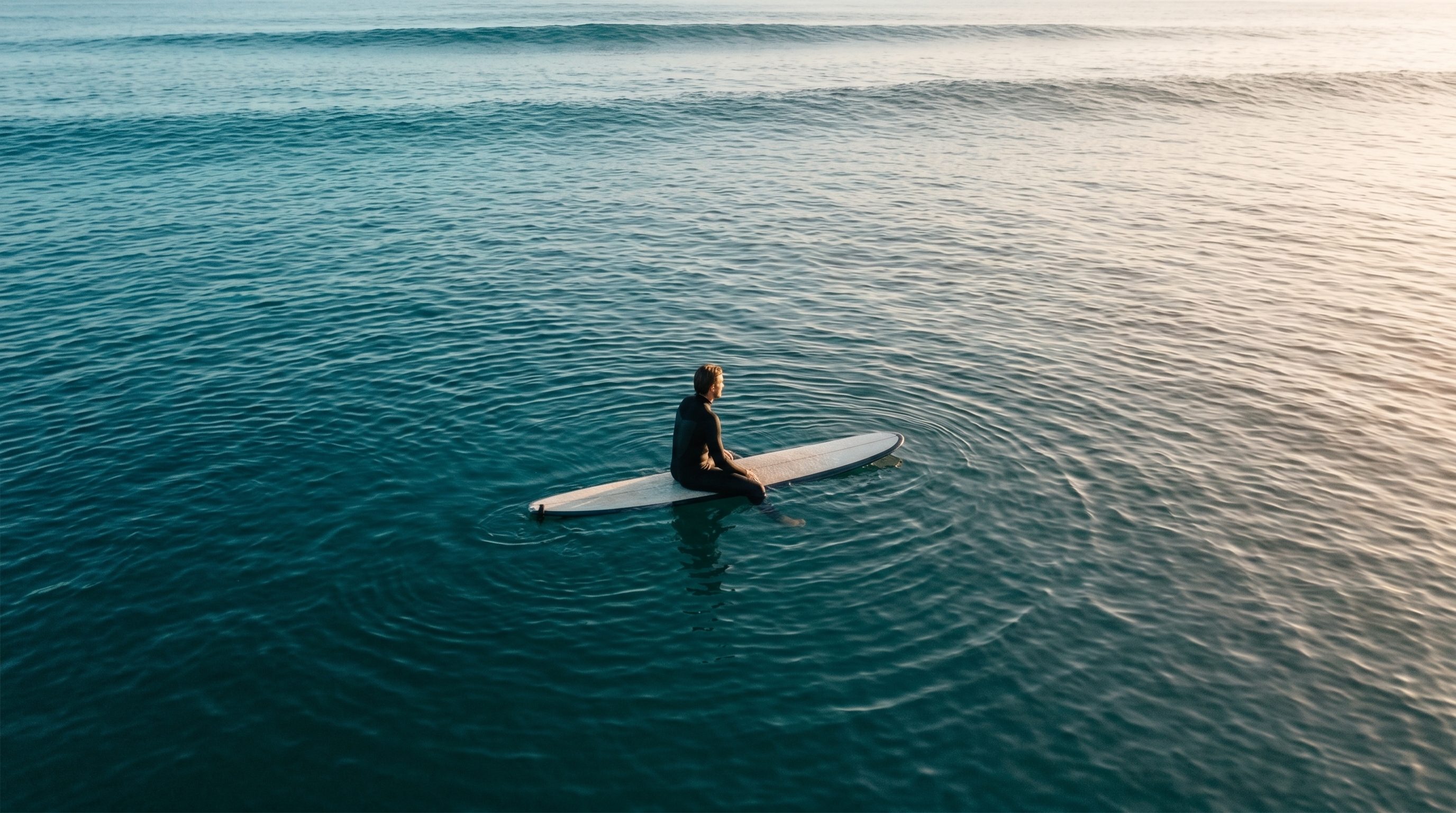 Vue aérienne d'un surfeur assis sur sa planche, contemplant l'horizon, eau calme