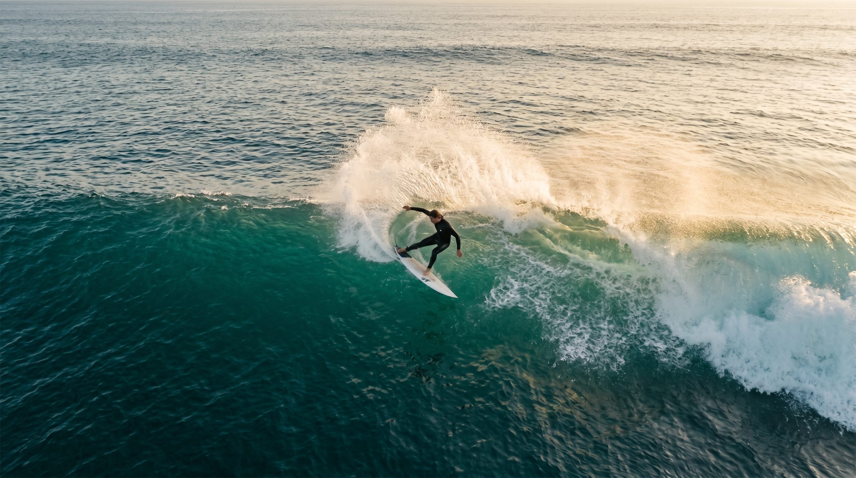 Vue aérienne d'un surfeur en pleine maîtrise sur une grande vague propre, embruns dans la lumière dorée