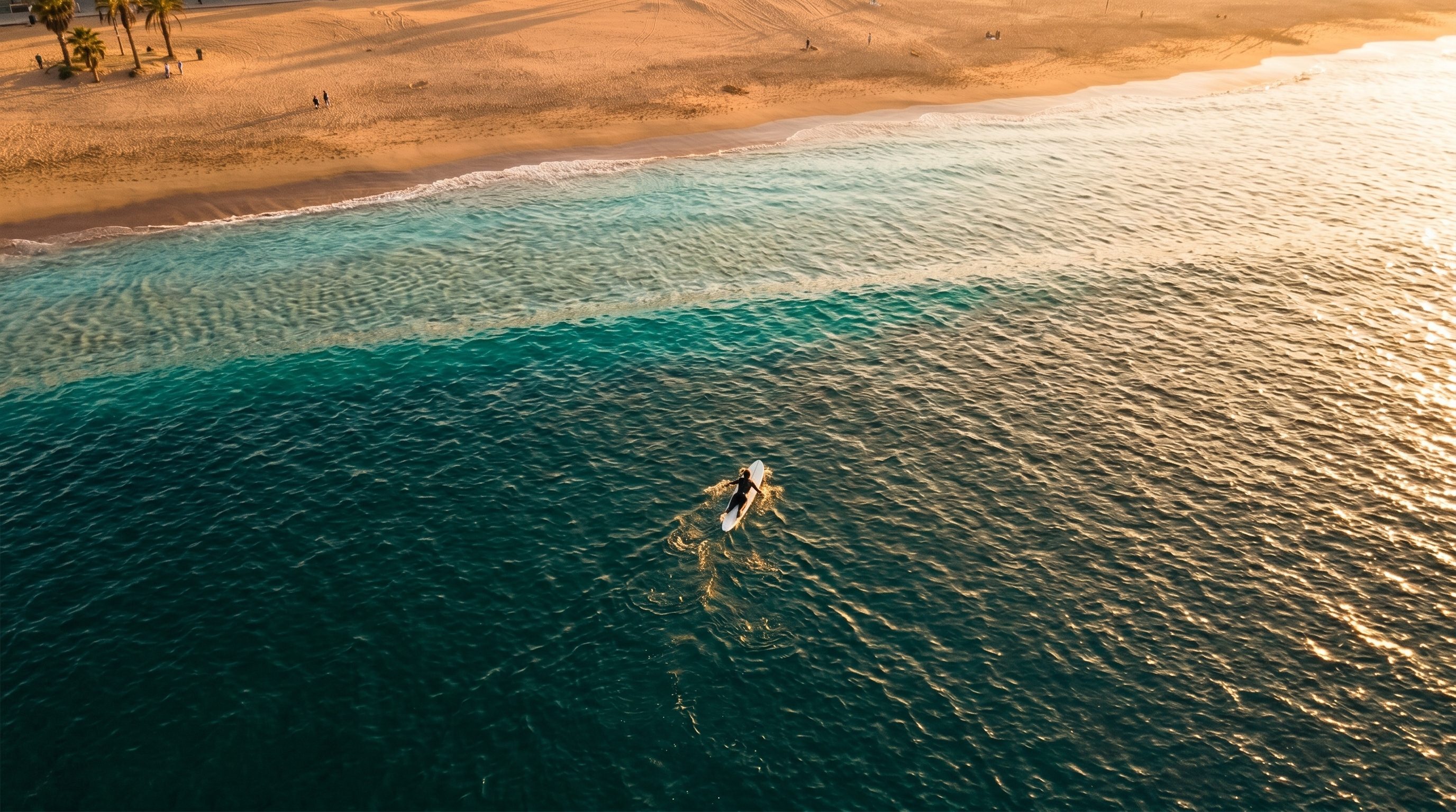 Vue aérienne d'un surfeur rentrant à la rame vers la plage, sable doré visible au loin